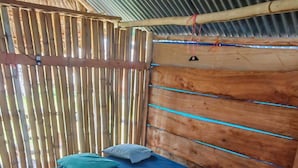A single bed with a blue mattress and pillows, wooden headboard, and a bamboo fence. - Pelicano Island (Moraquedub)