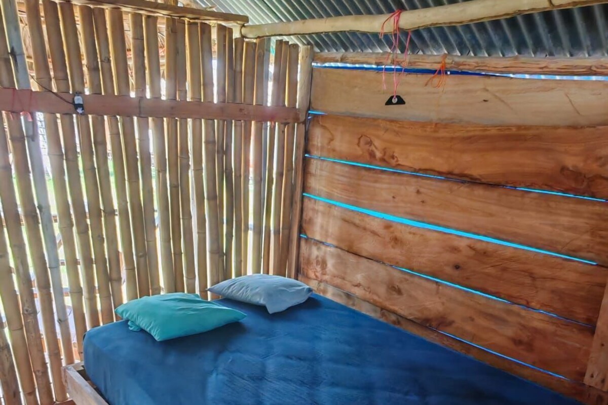 Una cama individual con colchón y almohadas azules, cabecero de madera y valla de bambú.