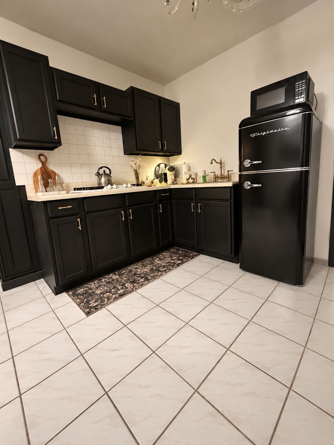 A kitchen with black cabinets, a black refrigerator, and a tiled floor.