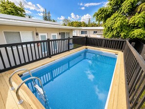 Ein rechteckiger Swimmingpool mit Holzdeck und Metallhandläufen, umgeben von einem schwarzen Zaun.