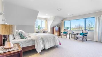 Un dormitorio con cama, mesita de noche, silla, una pequeña mesa y ventana con vistas.