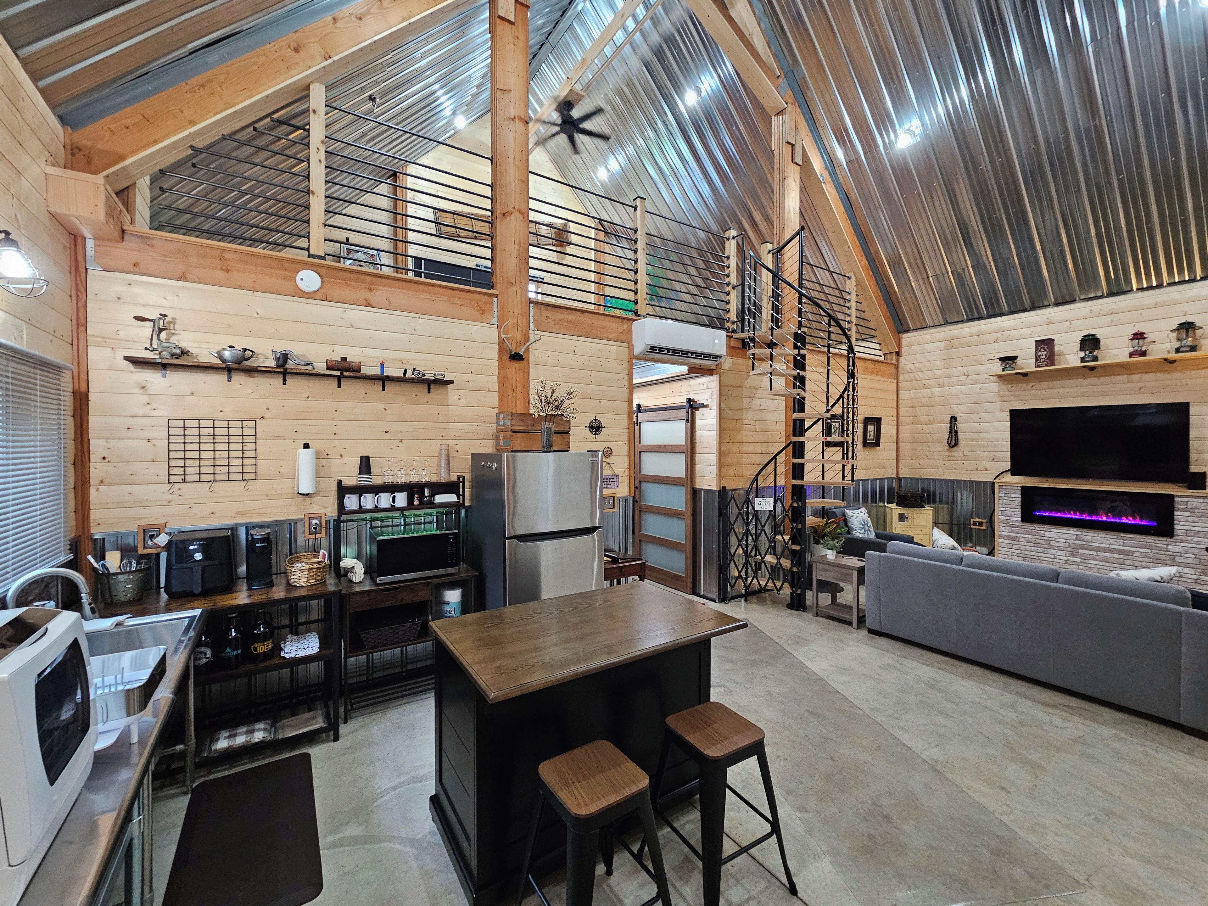 Cozinha ampla com ilha central, área de refeições com sofá e sala de estar com televisão e lareira.