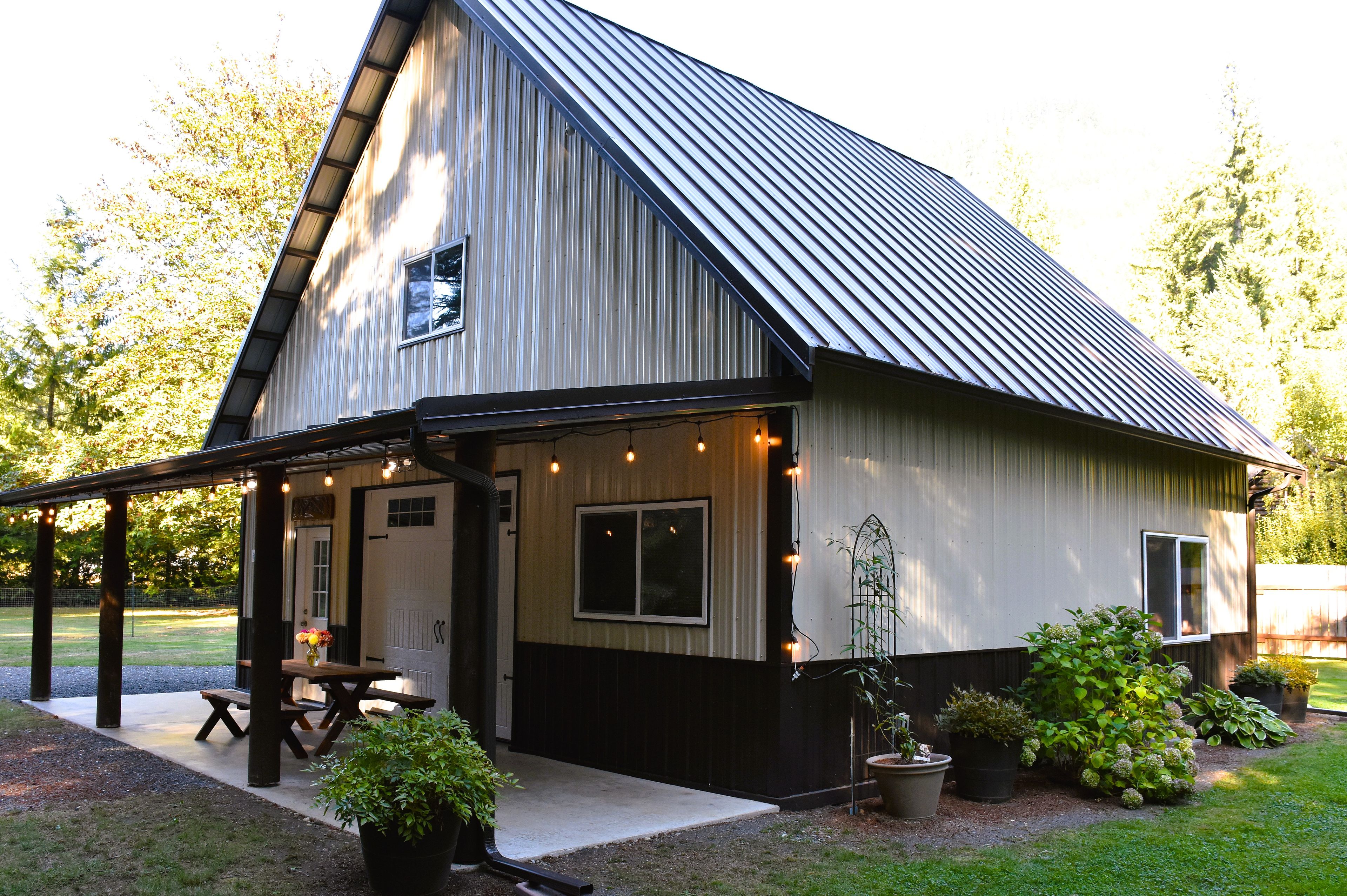 A two-story barn-style building with a covered porch, a picnic table, and potted plants.