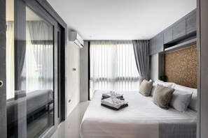 A modern hotel room with a large bed, a sliding glass door, and a view of the city. - Kamala - Peaceful Courtyard (Kathu District)