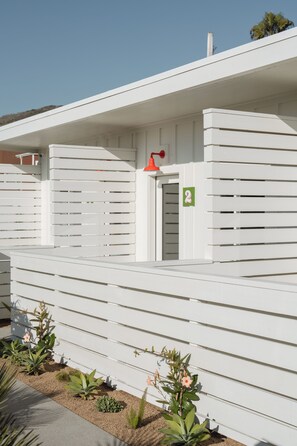 A white building with horizontal slats, a door with a number sign, and a small window.