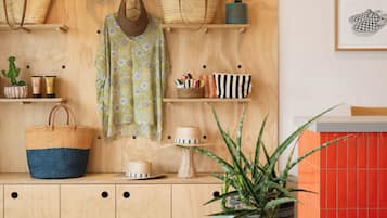 Ein Zimmer mit einer Holzwand, auf der Taschen, ein Hut und eine Pflanze ausgestellt sind. Es gibt einen runden Tisch mit Büchern und einer Topfpflanze.