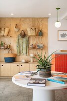 A room with a wooden wall displaying bags, a hat, and a plant. There's a round table with books and a potted plant.