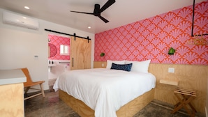 A bedroom with a bed, a desk, a chair, a ceiling fan, and a wall with a patterned wallpaper. - Two Palms Motel (Cayucos)