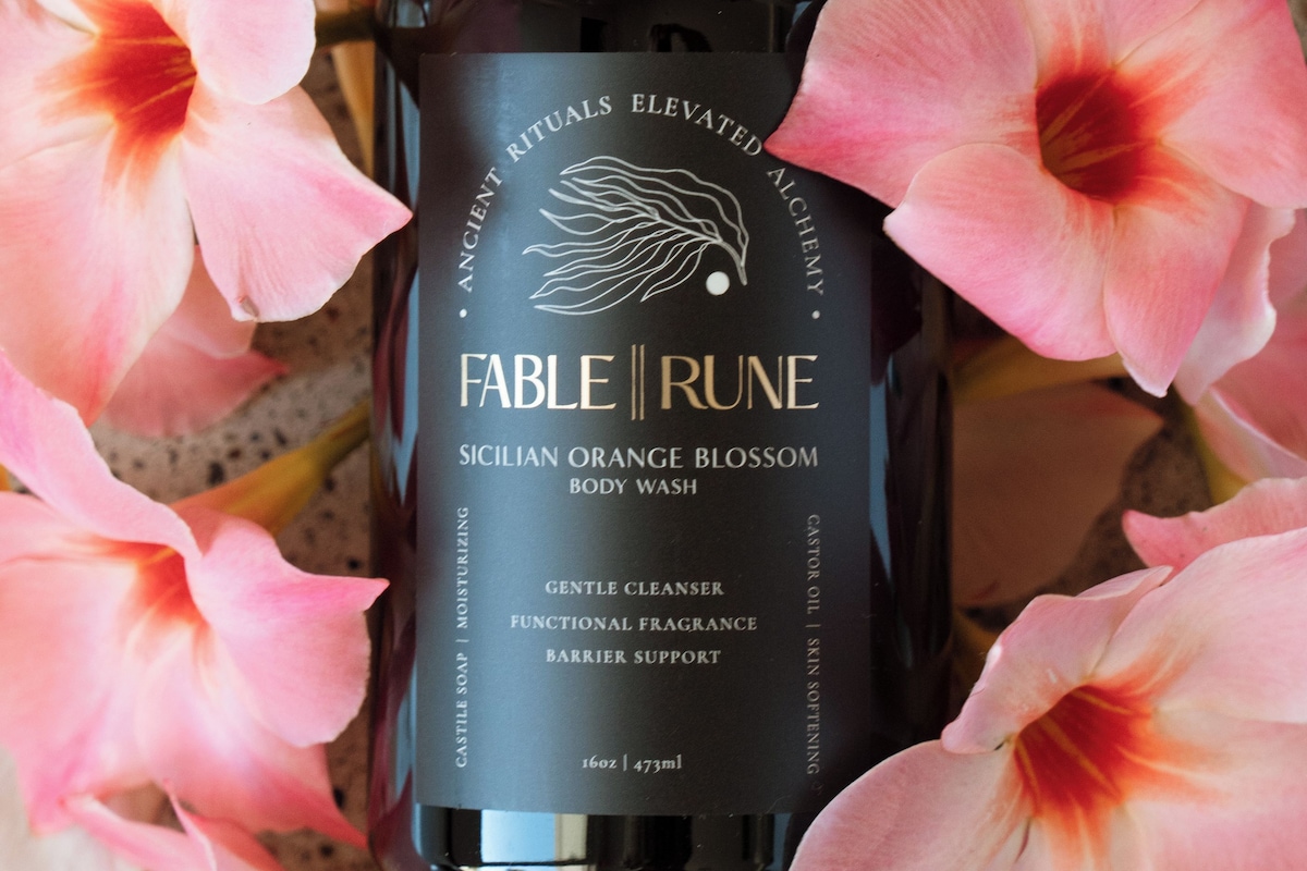 A bottle of Fable Rune body wash surrounded by pink flowers.