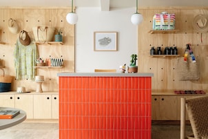 Una habitación con una pared de madera, un panel naranja en el centro y varios objetos como bolsos, un sombrero y un cuadro enmarcado.