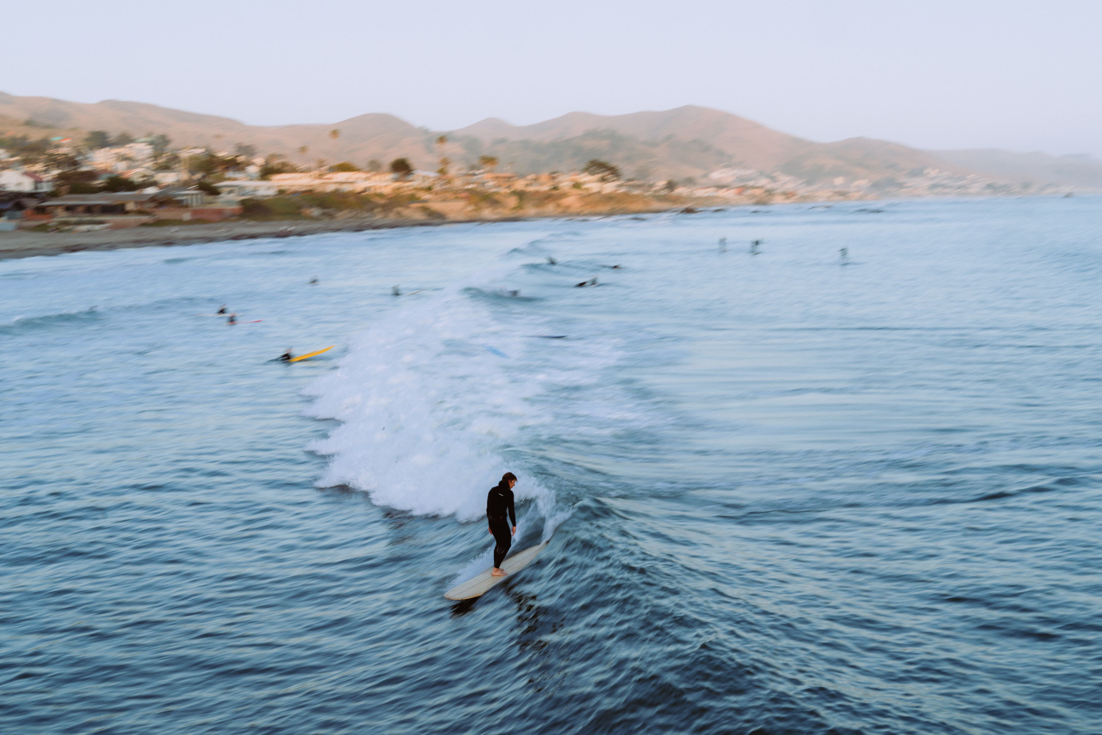 A person surfing on a wave in a coastal area with mountains in the background.