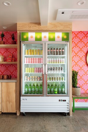 A beverage refrigerator stocked with various drinks, including bottles and cans, in a room with a patterned wall and wooden shelves.