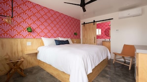 A bedroom with a bed, a desk, a chair, a ceiling fan, and a bathroom visible through a sliding door. - Two Palms Motel (Cayucos)