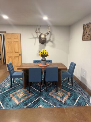 A dining area with a wooden table, blue upholstered chairs, a patterned rug, a wall-mounted deer head, and a clock. - Tranquil 2-bedroom house with AC in charming Stephenville (Stephenville)