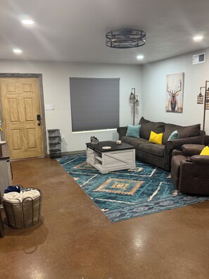 A living room with a brown leather sofa, a coffee table, a patterned rug, and a door. - Tranquil 2-bedroom house with AC in charming Stephenville (Stephenville)