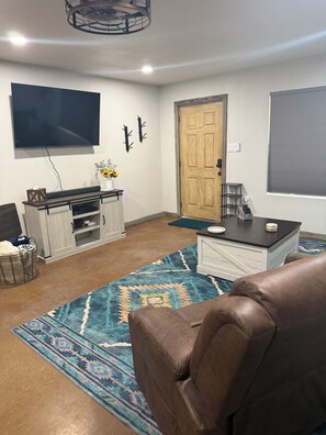 Ein Wohnzimmer mit einer braunen Ledersofa, einem an der Wand befestigten Flachbildfernseher, einer Holztür und einem gemusterten Teppich.
