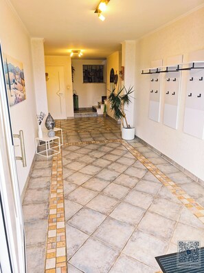 Un couloir avec un sol carrelé, un escalier et un porte-manteau fixé au mur.