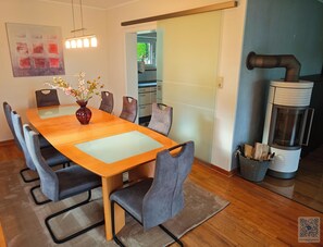 Un coin repas avec une table en bois, des chaises à revêtement gris, un vase avec des fleurs et, au fond, une cuisine moderne.
