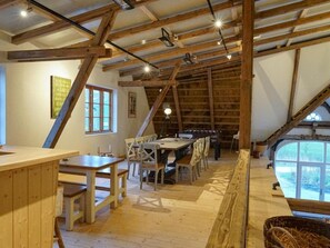 An attic room with a wooden table and chairs, a large window, and exposed wooden beams. - Kohstall in the Haubarg Ossenhoff (Tating)