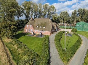 A large house with a thatched roof, surrounded by a well-maintained lawn and a curved driveway. - Kohstall in the Haubarg Ossenhoff (Tating)