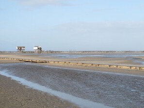 A coastal area with a sandy beach, a pier, and two white buildings. - Kohstall in the Haubarg Ossenhoff (Tating)
