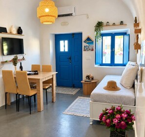 A room with a dining table, chairs, a sofa, a TV, a blue door, a window with blue shutters, and a wall-mounted air conditioner. - Casa Calma House (Emporio)