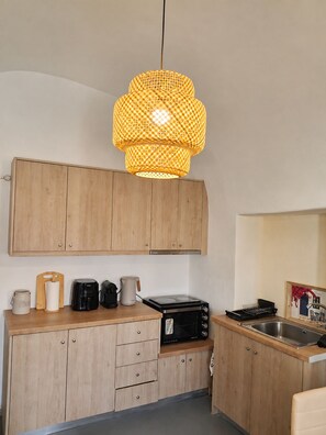 Een moderne keuken met houten kastjes, een magnetron, een koffiezetapparaat en een hanglamp.