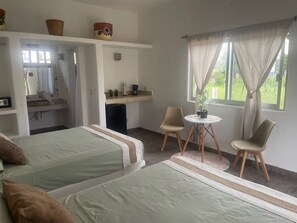 Een kamer met twee bedden, een tafeltje met stoelen, een wastafel en een raam met gordijnen.