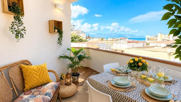 Un balcón con una mesa de comedor para cuatro personas, rodeado de muebles de mimbre y plantas en macetas.
