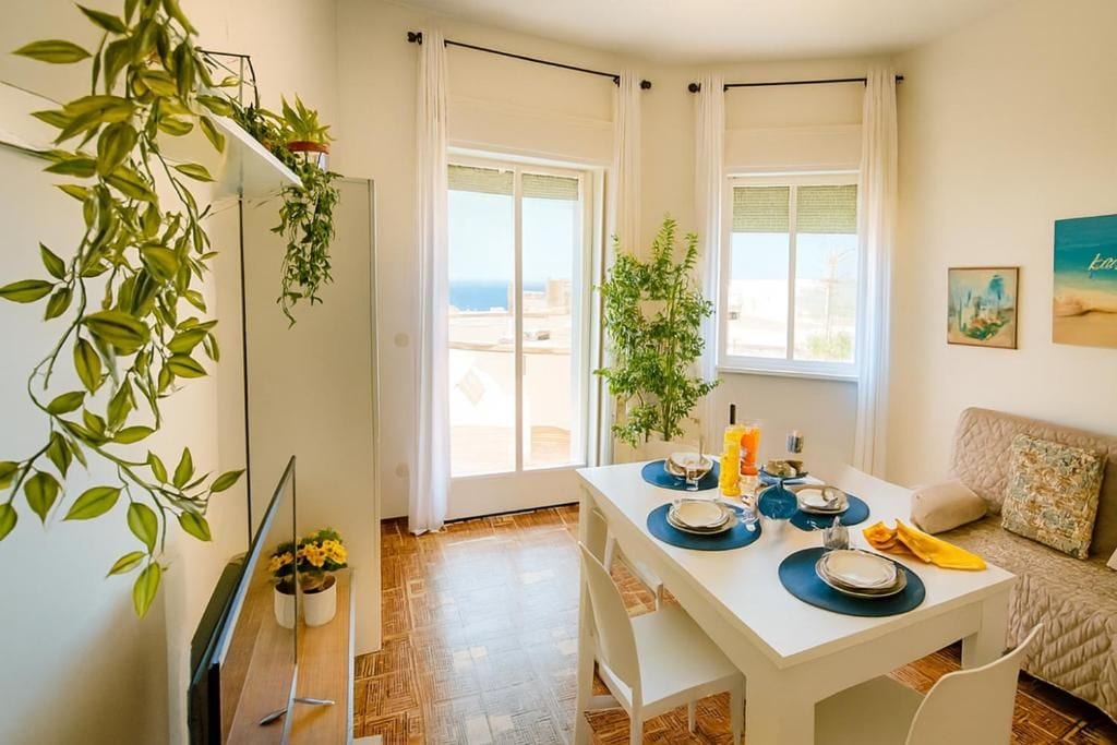 A dining area with a table set for two, a sofa, and a view of the outdoors.