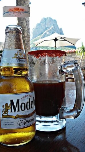 Una botella de cerveza Modelo Especial y un vaso con borde rojo, sobre una mesa con vista a la montaña.