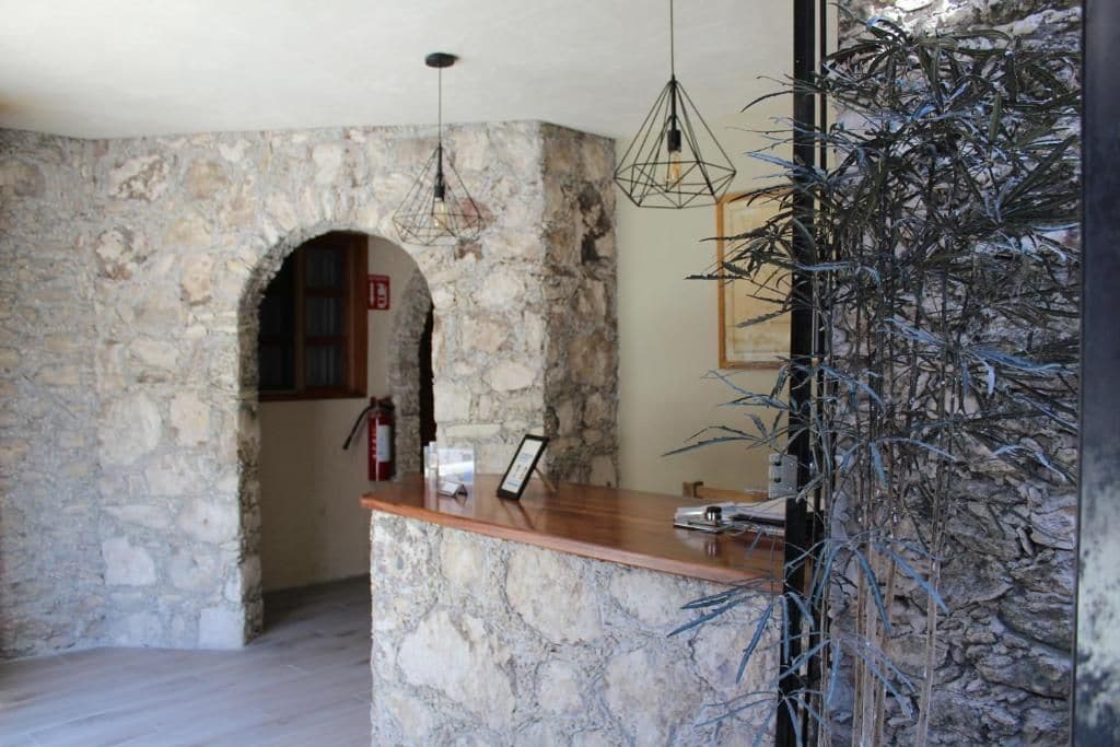 Una zona de recepción con pared de piedra, mostrador de madera, luces colgantes y un cuadro enmarcado.
