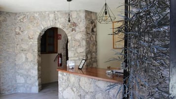 Una zona de recepción con pared de piedra, mostrador de madera, luces colgantes y un cuadro enmarcado.