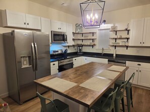 A modern kitchen with a stainless steel refrigerator, a microwave, a stove, and a sink. There are wooden cabinets and a wooden dining table with chairs. - Cozy 2-bedroom  new house in tranquil Eclectric. (Eclectic)