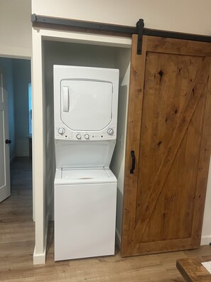 A white washer and dryer unit with a wooden barn-style door in a laundry room. - Cozy 2-bedroom  new house in tranquil Eclectric. (Eclectic)