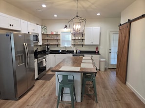 A modern kitchen with a central island, stainless steel appliances, and a farmhouse-style door. - Cozy 2-bedroom  new house in tranquil Eclectric. (Eclectic)