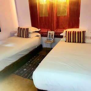 A hotel room with two single beds, a small table with a lamp, and a wooden headboard with a mirror. - Riad Rêve D'antan Dream (Marrakech)