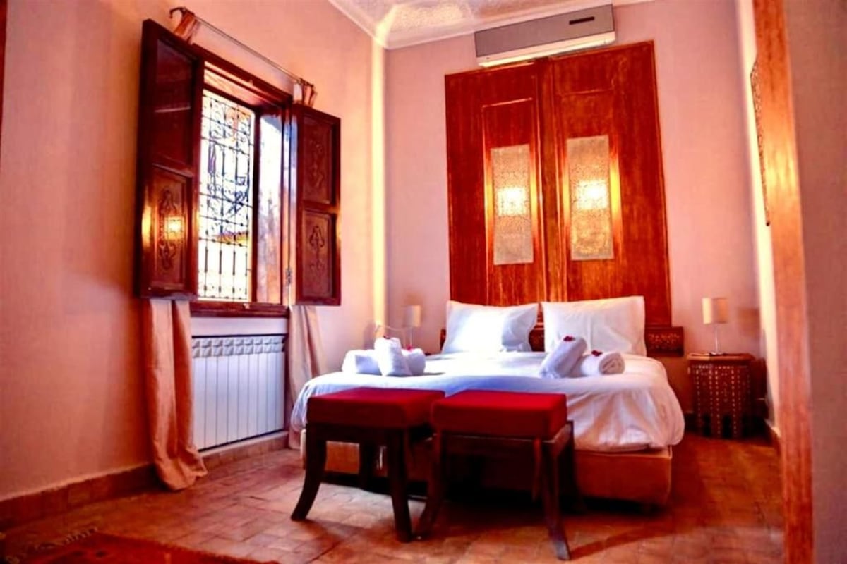 A hotel room with a large bed, two bedside tables, a window with curtains, and a radiator.