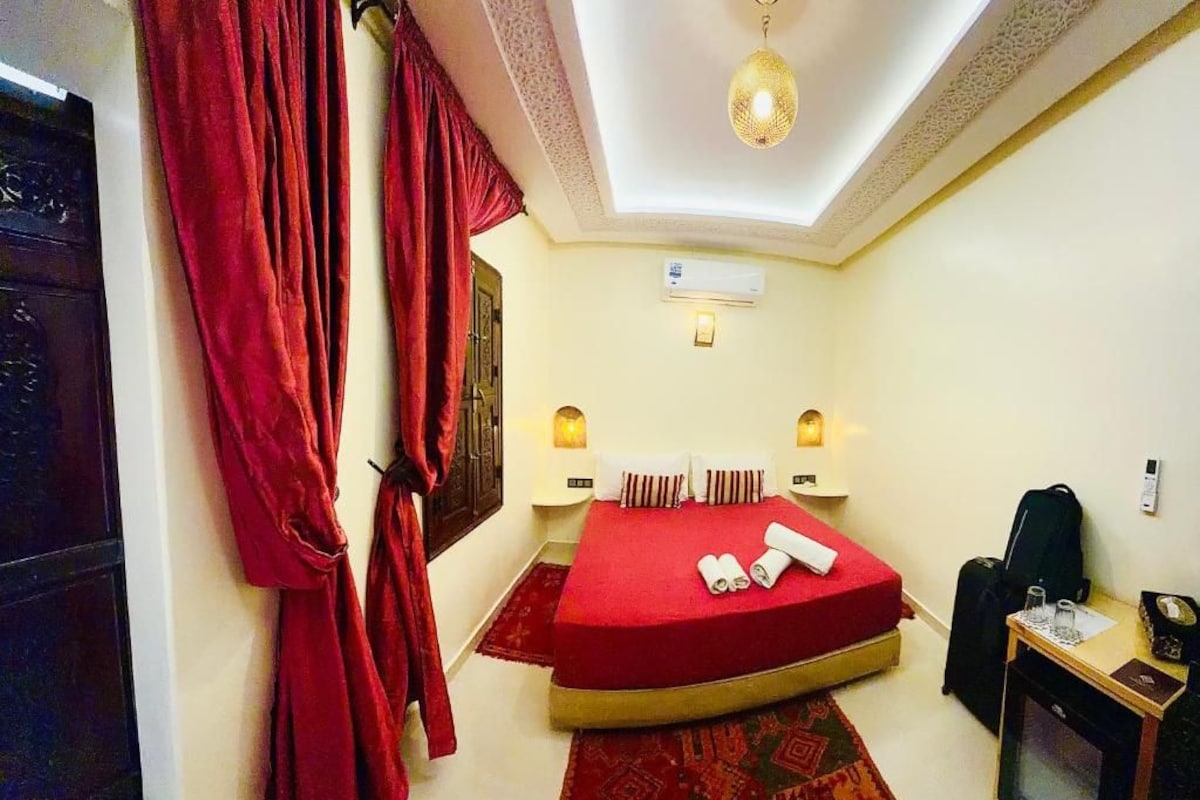 A hotel room with a bed, a desk, an air conditioning unit, and a television.