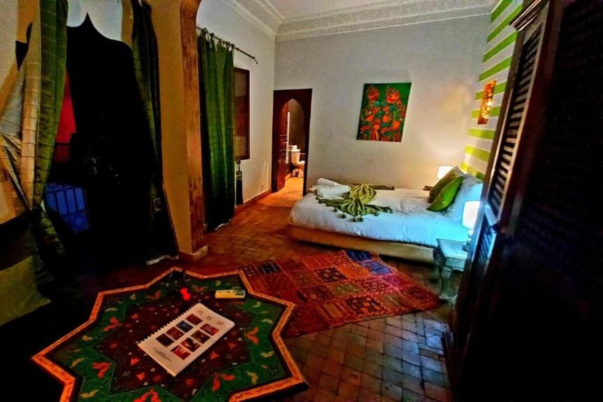 A room with a bed, a window with curtains, a wall with a painting, and a patterned rug on the floor.