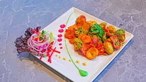 A square white plate with a colorful vegetable dish, garnished with red onion, green herbs, and yellow dots. - Sunday Hotel by CheckIn Greater Noida (Greater Noida)