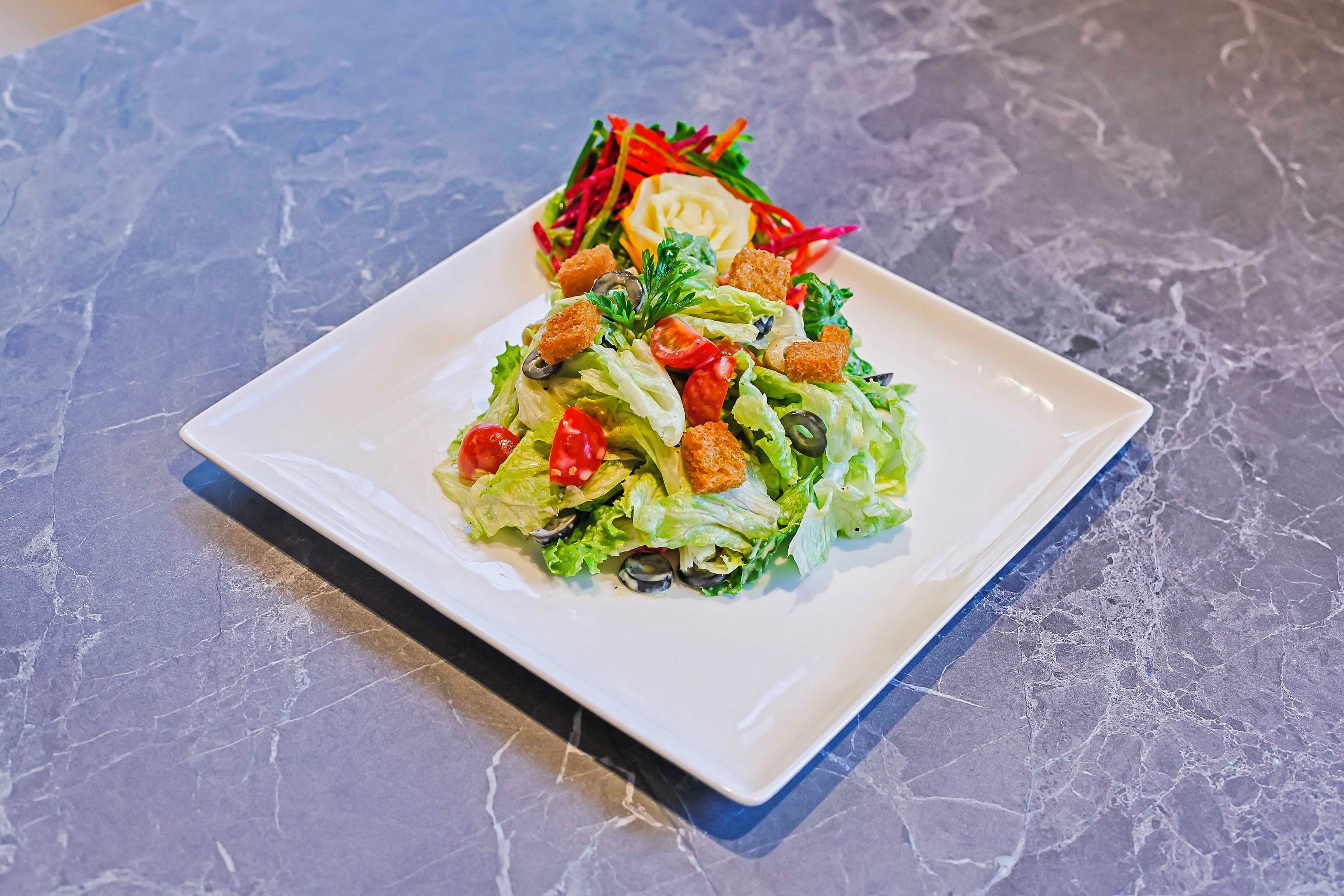 Un plato blanco rectangular con una ensalada sobre una superficie de mármol.