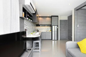 A modern kitchen with a built-in stove, a refrigerator, and a dining area with a white table and bar stools. - Kamala - Green Jungle View (Kathu District)