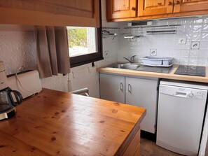 A kitchen with wooden cabinets, a stainless steel sink, a dishwasher, and a window with curtains. - Peisey-Loue: Apartment at the base of the slopes, sleeps 6 (Peisey-Nancroix)