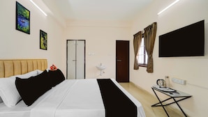 Quarto de hotel com cama, mesa de cabeceira com chaleira, televisão e janela com cortinas.