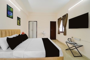 A hotel room with a bed, a bedside table with a kettle, a TV, and a window with curtains. - Palette Legacy Apartment-Saravanampatti (Coimbatore)