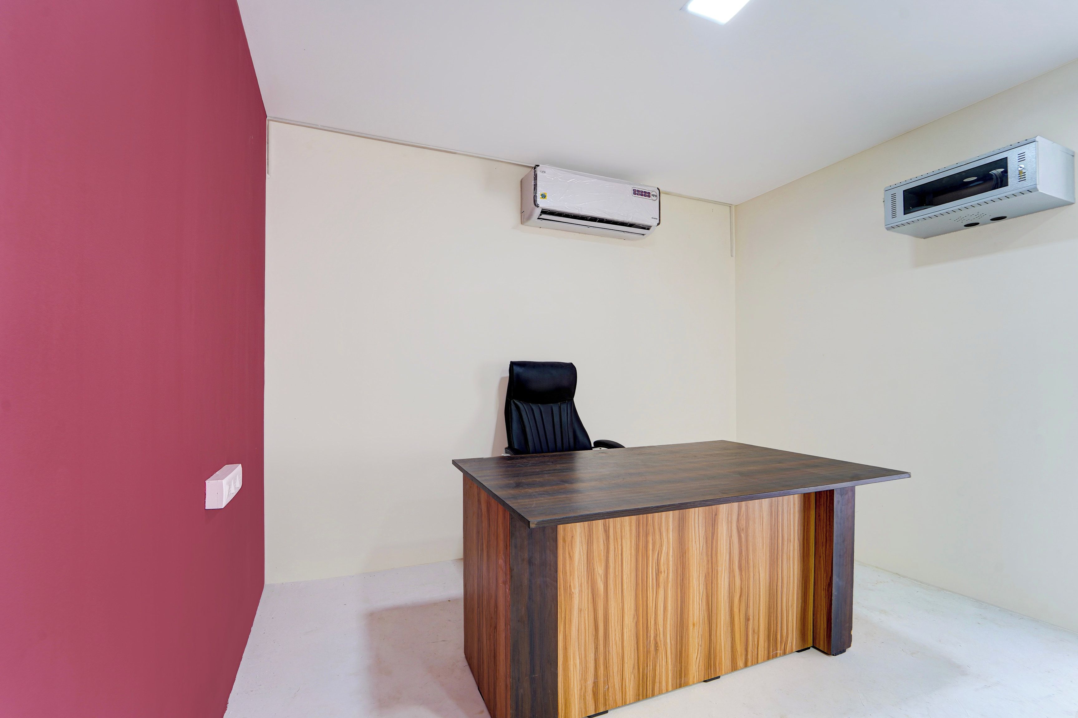 Una habitación con un escritorio de madera, una silla de oficina negra y dos unidades de aire acondicionado instaladas en la pared.