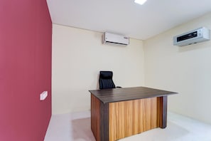A room with a wooden desk, a black office chair, and two air conditioning units mounted on the wall.