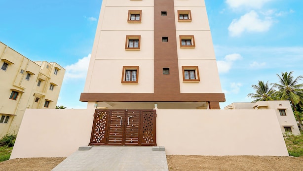 Um edifício com vários andares, painel vertical marrom central, janelas em cada andar e um portão decorativo na entrada.