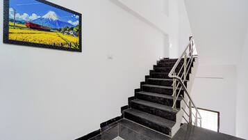 Una escalera con escalones negros y barandilla metálica, que lleva a un rellano con un cuadro enmarco de un paisaje.